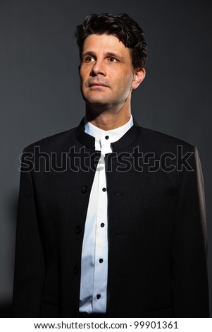 Wise man in black costume with white shirt isolated on dark background. Studio portrait.