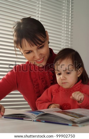 A beautiful Caucasian mother and daughter holding book on a light background