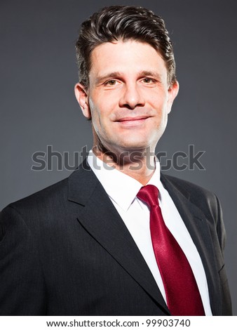 Smiling business man with dark grey suit and red tie isolated on dark background. Studio shot.