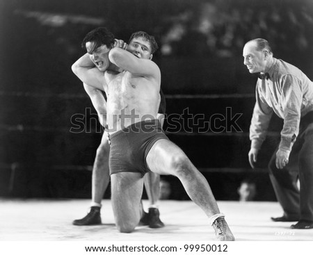 Two men wrestling with referee making a call in the background