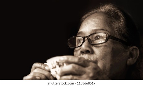 Image Of 60s Or 70s  Asian Elderly Drinking Tea.Old Woman Wearing Eye Glasses,lonely With Cold Cup.She Looking Outside Or Flew Away ,Vintage Film Color Tone.Sad Elderly Concept.Sepia Color Tone