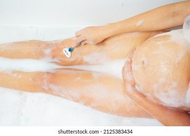 Image from above of a pregnant woman shave leg with razor and holding tummy
