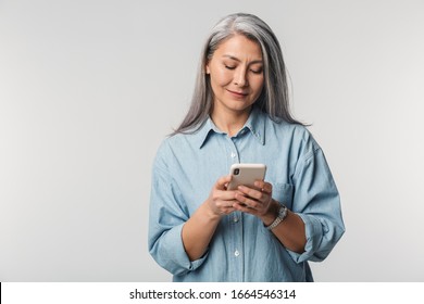 Image of adult mature woman with long white hair wearing shirt holding cellphone isolated over gray background