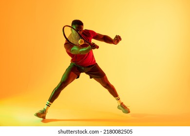 Image of african american male tennis player hitting ball in yellow lighting. Sport, movement, fitness and active lifestyle concept. - Powered by Shutterstock