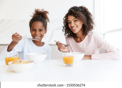 Image of african american woman and her little daughter having breakfast and eating corn flakes in kitchen