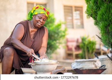 image of African mother cooking from  a compound house-black woman preparing dish in an open space-mother stirring food on fire with great joy and happiness.