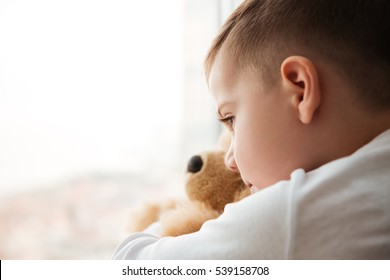 Image of alone little boy with teddy bear near window waiting for parents at home. Look at window. - Shutterstock ID 539158708
