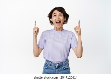 Image Of Amazed, Super Happy Girl Looking With Fascinated, Astonished Face Up, Pointing Fingers At Logo, Sale Promo, Showing Advertisement, White Background