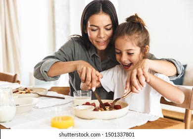 Image of amazing family mother and little daughter smiling and eating tasty food together while having breakfast at home in morning - Powered by Shutterstock