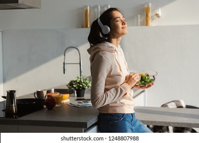 Image Of An Amazing Happy Healthy Woman In The Kitchen Standing Daily Morning Routine Eat Salad Listening Music In Headphones.