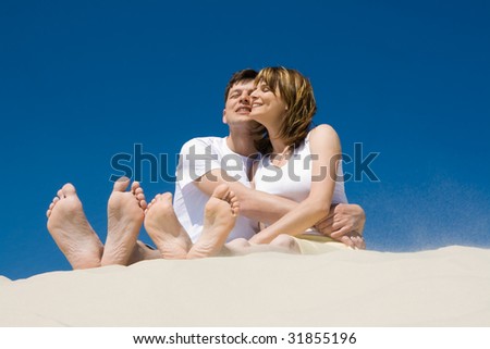 Image of amorous couple sitting on sandy beach and enjoying hot day