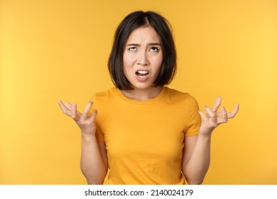 Image of angry asian woman, shouting and cursing, looking outraged, furious face expression, standing over yellow background - Shutterstock ID 2140024179