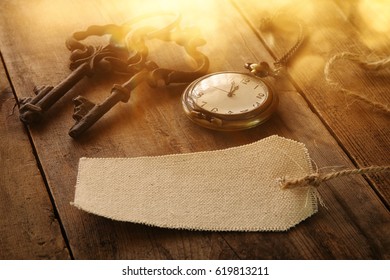 Image of antique keys, empty canvas tag and pocket clock on old wooden table
