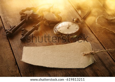 Image of antique keys, empty canvas tag and pocket clock on old wooden table