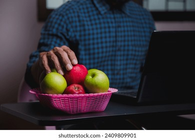 Image of an apple placed on a desk, a man's computer in a green plaid shirt. - Powered by Shutterstock