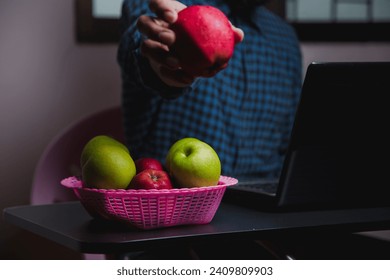 Image of an apple placed on a desk, a man's computer in a green plaid shirt. - Powered by Shutterstock