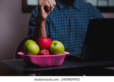 Image of an apple placed on a desk, a man's computer in a green plaid shirt. - Powered by Shutterstock