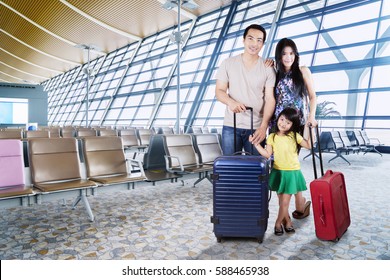 Image Of Asian Family Carrying Suitcases For Holiday While  Standing In The Airport Terminal 