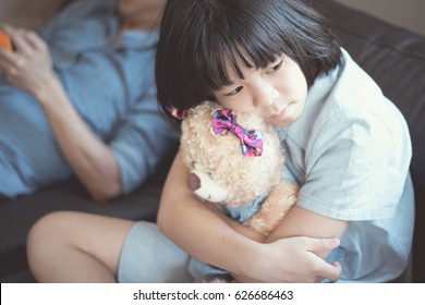 Image of Asian female kid sit on couch hug a bear sad looking outside while her father playing phone don't care for his daughter. Asian problem child girl depress from seeking attention from parents - Powered by Shutterstock