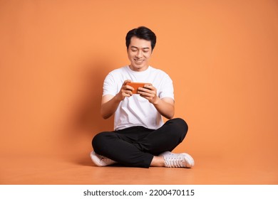 image of asian man sitting using phone and isolated on orange background - Powered by Shutterstock