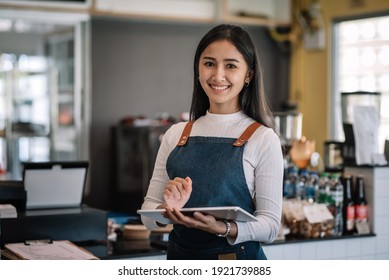 Image of an Asian woman barista wearing an apron at the café owner at the tablet. Looking at camera. - Powered by Shutterstock