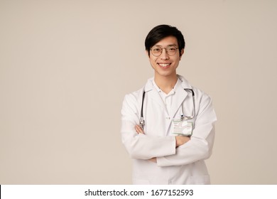 Image Of Asian Young Male Doctor In Medical White Uniform Smiling Isolated Over Beige Background