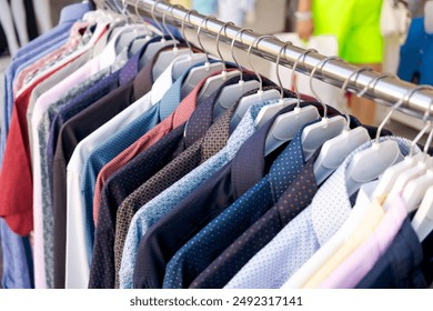 Image of assorted men's shirts in various colors and patterns on hangers in a store display. The background is blurred, focusing on the shirts. Concept of fashion retail and clothing - Powered by Shutterstock