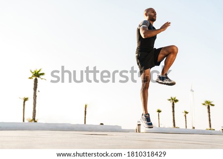 Image of athletic african american sportsman jumping while working out outdoors