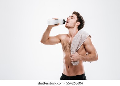 Image Of Attractive Athlete Standing With Towel Holding Bottle Of Water While Drinking Over White Background.