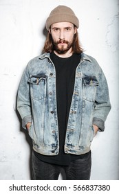 Image Of Attractive Bearded Hipster Man Wearing Hat Dressed In Jeans Jacket Posing Over Wall Background.