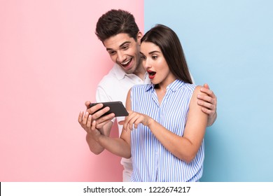Image of attractive couple 20s smiling and looking at mobile phone isolated over colorful background