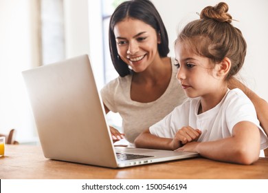 Image Of Attractive Family Woman And Her Little Daughter Smiling And Using Laptop Computer Together While Sitting At Table In Apartment