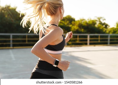 Image of attractive fitness woman wearing tracksuit and wristwatch running outdoors - Powered by Shutterstock