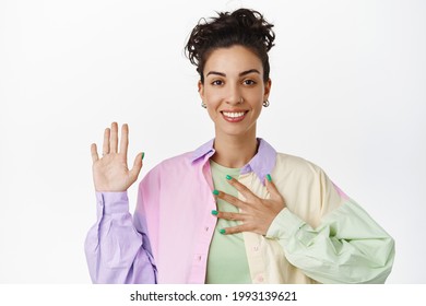 Image of attractive queer girl raising hand, holding hand on chest, introduce herself, volunteering, making promise, standing over white background