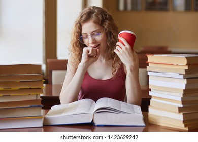 Image of attractive seepy student sitting in reading room and yawning, preparing for classes, work overtime, looks tired, drinking coffee, foxy haired female reads encyclopedia, finding information. - Shutterstock ID 1423629242