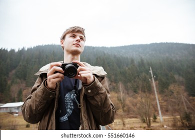 Image of attractive young man photographer make a photo by his camera in the mountains. Looking aside.
