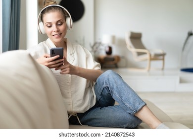 Image Of Attractive Young Woman In Headphones Holding Smartphone While Sitting On Sofa At Home