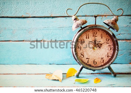 Image of autumn Time Change. Fall back concept. Dry leaves and vintage alarm Clock on a blue rustic wooden background