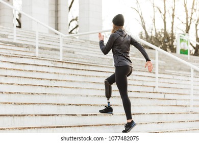 Image from back of energetic disabled girl with prosthetic leg in sportswear working out and running at the stairs in stadium - Powered by Shutterstock