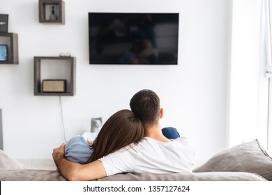 Image from back of happy couple man and woman in casual wear watching television on sofa at home - Powered by Shutterstock