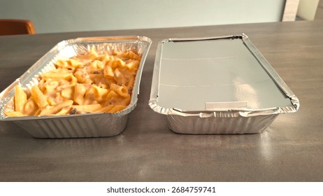 Image of batch cooked pasta bake that can be frozen and re-heated later. Homemade freezer meals in foil containers, one with lid on and one with lid off showing re-heatable pasta meal. Batch food prep