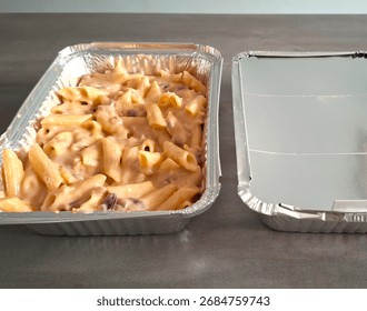 Image of batch cooked pasta bake that can be frozen and re-heated later. Homemade freezer meals in foil containers, one with lid on and one with lid off showing re-heatable pasta meal. Batch food prep