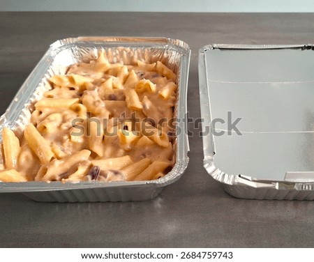 Image of batch cooked pasta bake that can be frozen and re-heated later. Homemade freezer meals in foil containers, one with lid on and one with lid off showing re-heatable pasta meal. Batch food prep