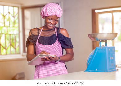 image of beautiful african lady in apron and head wrap, cheerful black woman with book- grocery list concept - Powered by Shutterstock