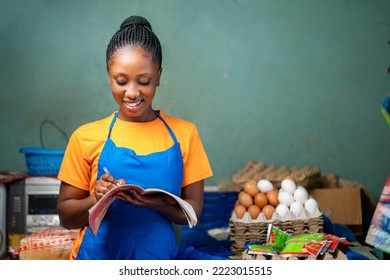 image of beautiful african lady with a book, food products sorrounded her- shopkeeper taking stock