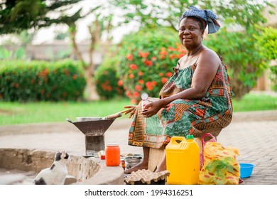 image of beautiful african mother sitting outside cooking- cheerful black woman preparing food with containers and plastics around her