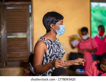 image of beautiful African teacher-black tutor in class room wearing face mask after covid-19 lock down with pupils blurred at background