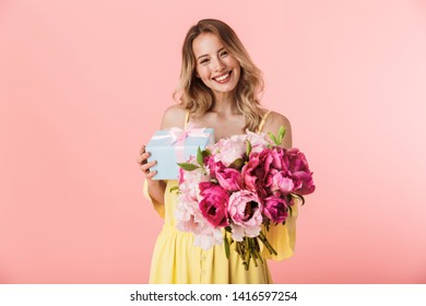 Image Of A Beautiful Amazing Young Blonde Woman Posing Isolated Over Pink Wall Background Holding Flowers Holding Present Gift Box.
