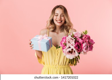 Image Of A Beautiful Amazing Young Blonde Woman Posing Isolated Over Pink Wall Background Holding Flowers Holding Present Gift Box.