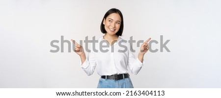 Image of beautiful asian woman pointing fingers left and right, making decision, showing two variants choices, standing over white background